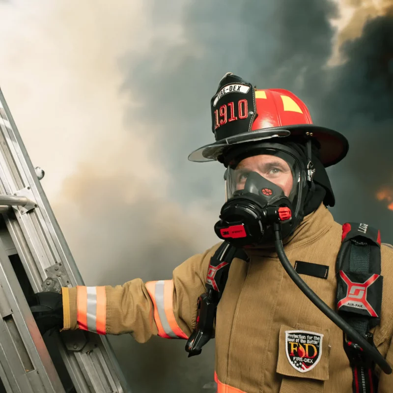 Firefighter wearing Fire-Dex® FXC Economical Turnouts in tan during operation, demonstrating full protective coverage, mobility, and reflective safety features in use.