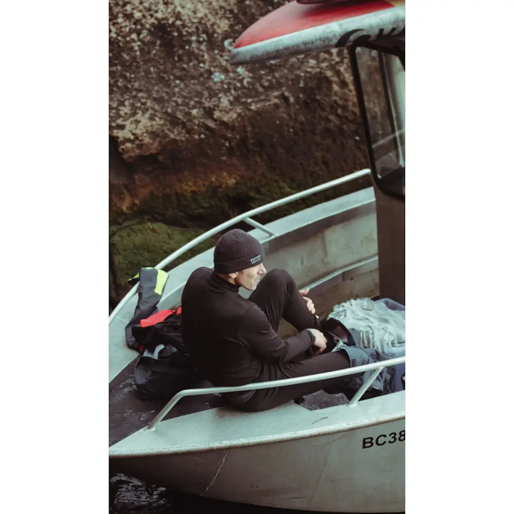 Man sitting in a boat wearing a Mustang Survival® Men’s Kazan Dry Suit Liner for warmth and comfort during cold-water conditions.