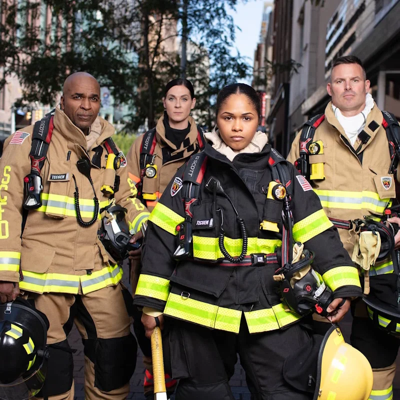 Four firefighters wearing Fire-Dex AeroFlex turnout gear in tan and black variants, fully geared with helmets, gloves, and utility belts.