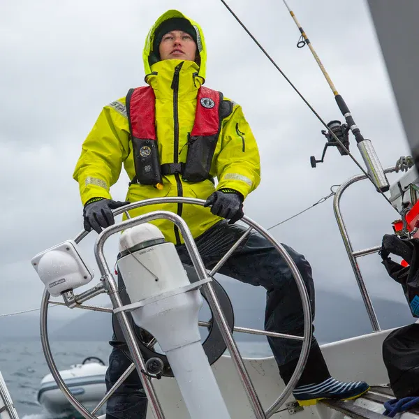 Fisher wearing Mustang Survival® HIT Hydrostatic Inflatable PFD in red/black variant while on a boat, hydrostatic automatic inflatable life jacket designed for boating and marine safety.
