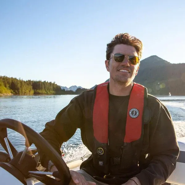 Person on a boat wearing the Mustang Survival® HIT Hydrostatic Inflatable PFD in red/black variant, a hydrostatic automatic inflatable life jacket for marine and boating safety.