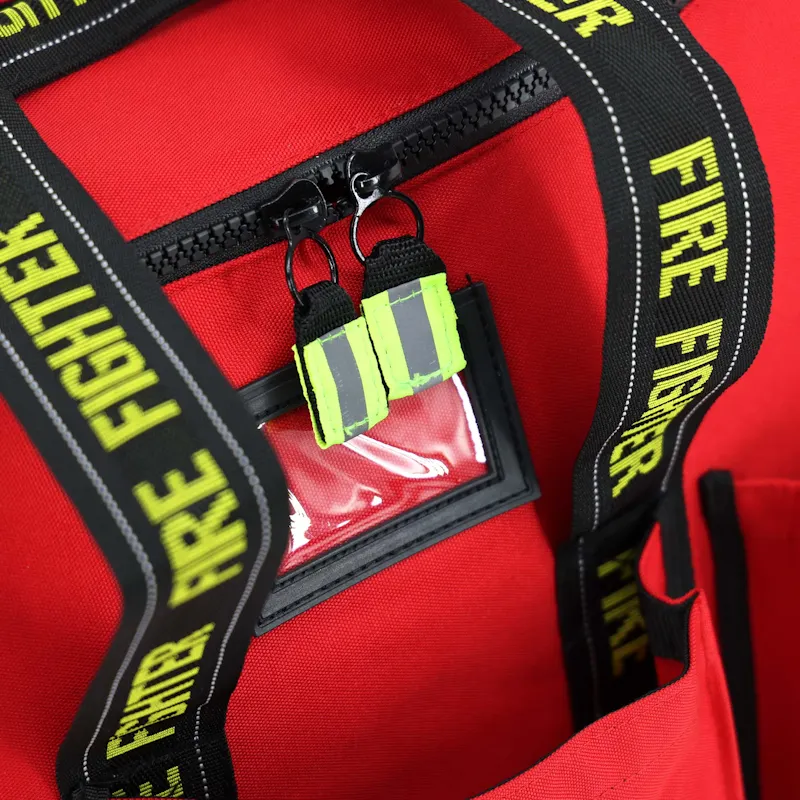 Close-up of the red Lightning X LXFB20 turnout gear bag's zipper with reflective pull tabs and clear ID window between Fire Fighter webbing handles.