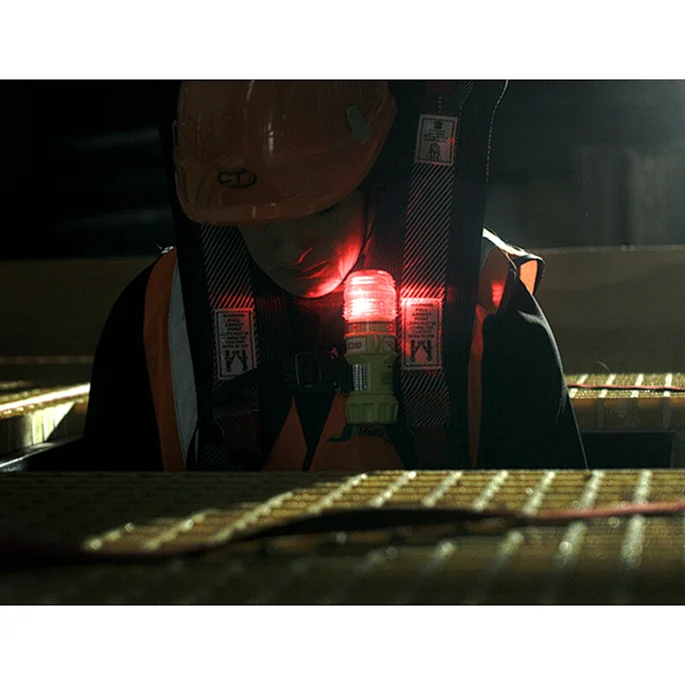 Eflare UB280 rechargeable LED safety beacon with red flashing light clipped to a worker's safety harness in a low-light industrial setting.