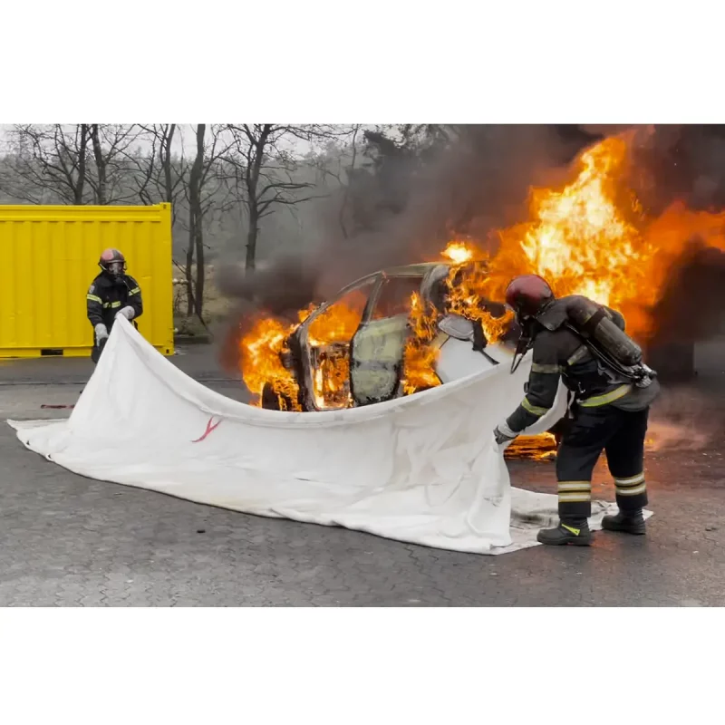 T-ISS FI-BL0906 EV Fire Blanket in use by two firefighters covering a burning vehicle — high-temperature silica fire blanket being deployed to safely isolate and suppress an electric vehicle fire, minimizing heat and smoke exposure.