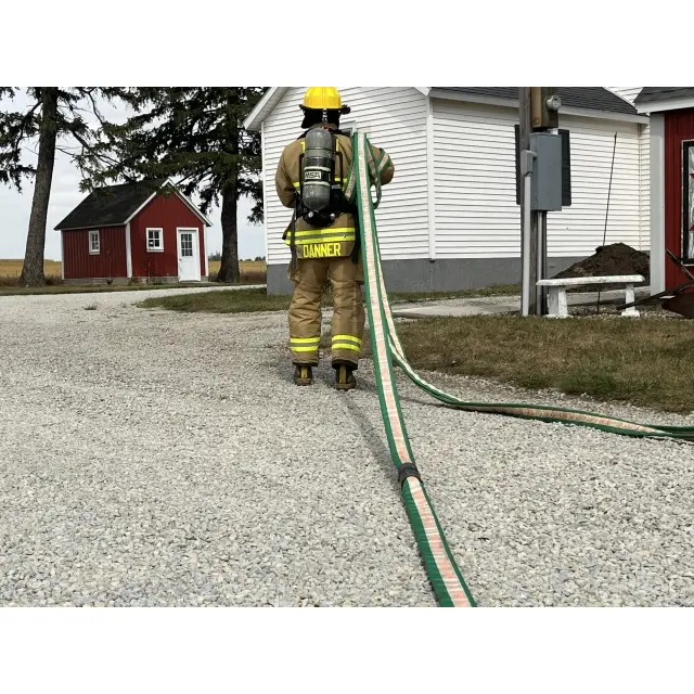 Firefighter holding the BullDog™ Hi-Combat® Firefighting Hose, looking toward a house, prepared for firefighting and rescue operations.