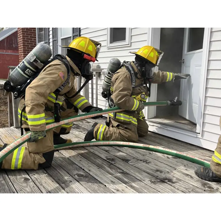Two firefighters kneeling at the front porch door holding the BullDog™ Hi-Combat® Firefighting Hose, ready to enter and combat a fire inside a smoke-filled home.