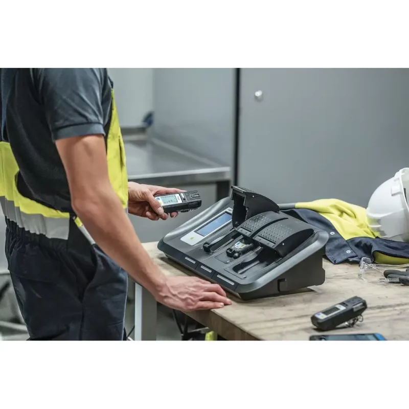 Worker holding the Dräger X-am® 5800 Multi-Gas Detector while another unit rests on a nearby table in an industrial setting.