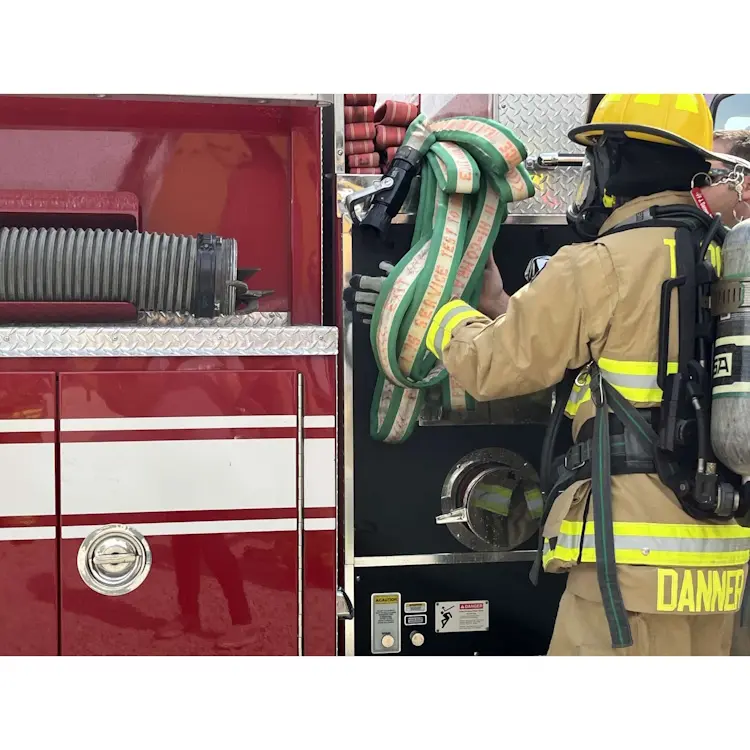 Folded BullDog™ Hi-Combat® Firefighting Hose neatly stored on a firetruck, with a firefighter reaching to grab it, prepared for immediate deployment.