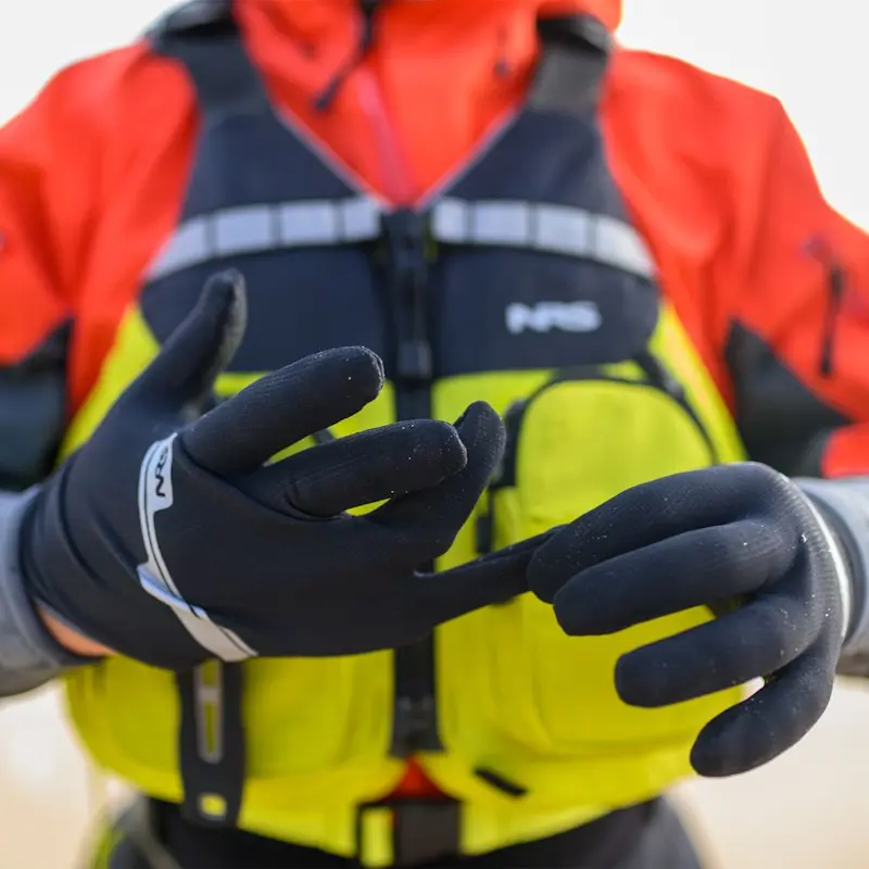 Close-up of a person wearing NRS Men's HydroSkin Gloves pulling on a fingertip, highlighting the flexible neoprene material, textured grip, and snug performance fit for cold-water activities.