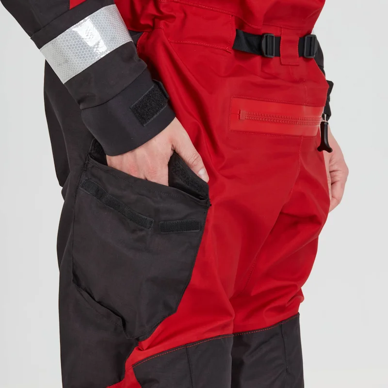 Closeup of a man wearing the NRS Ascent SAR Dry Suit in red with hands in pockets, highlighting the waterproof pocket design and suit fit.