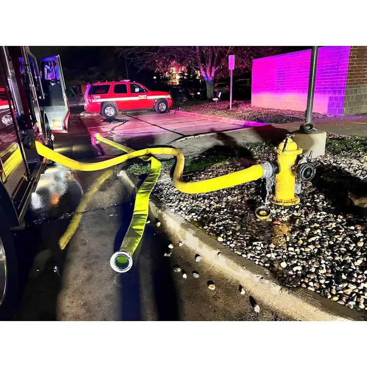Yellow BullDog™ Hi-Combat® Firefighting Hose connected to a hydrant and in active use at a fire scene with a firetruck present.