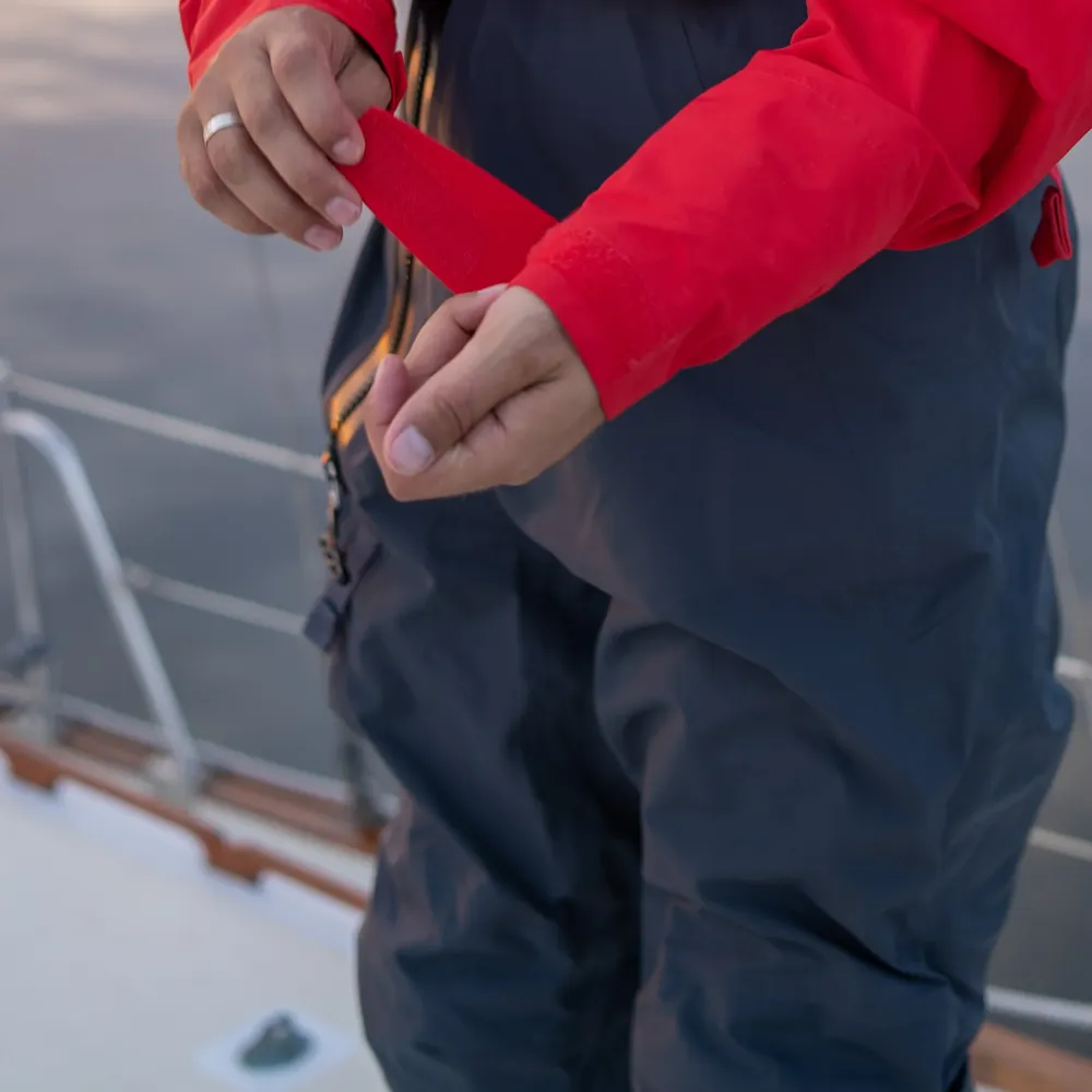 Closeup of a man tightening the Velcro wrist straps on the Mustang Survival® Men’s Hudson CCS Dry Suit in Admiral Red, showing detailed waterproof fabric and secure gasket seals.