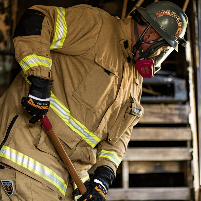 Firefighter in tan turnout gear and a half-mask respirator wearing Fire-Dex® Dex-Rescue NFPA 1951 Technical Rescue Firefighter Gloves while gripping a tool handle.