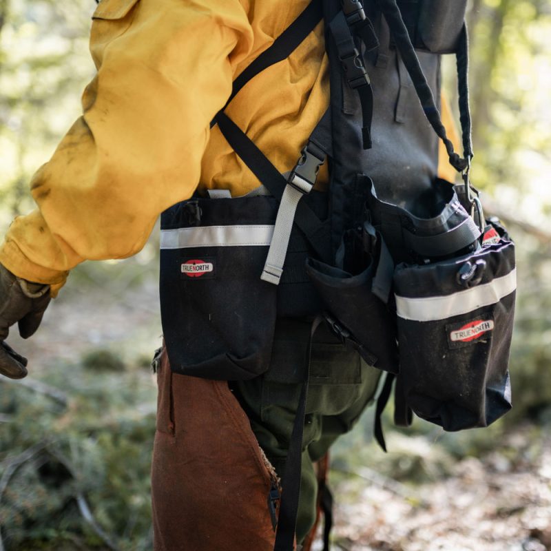 Close-up side view of person wearing True North Gear Chainsaw Pack highlighting padded shoulder straps, storage pockets, and chainsaw secured on the side.
