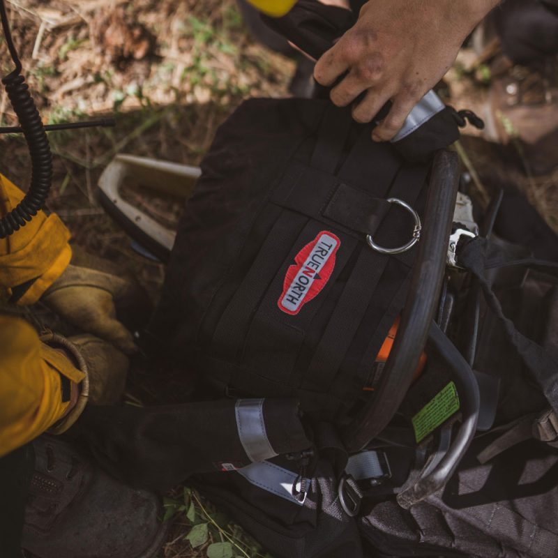 Close-up of True North Gear Chainsaw Pack resting on the ground, showing durable fabric, reinforced straps, and secured chainsaw holder.