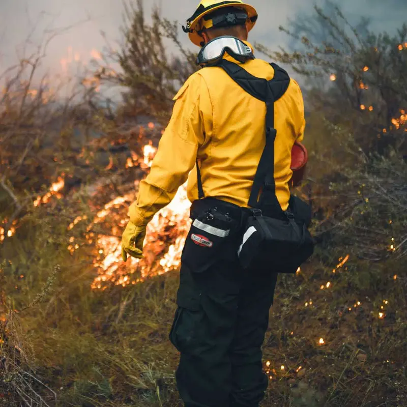 Alternate view of a firefighter wearing the True North Gear Spyder™ Gear Pack amid a forest fire, emphasizing the pack’s sturdy construction and functional design for reliable gear transport in intense wildfire environments.
