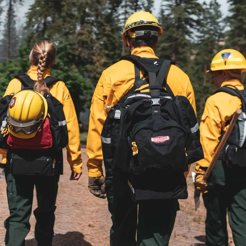 Multiple firefighters equipped with the red True North Gear Spitfire™ Pack, demonstrating coordinated wildfire response with durable, ergonomic packs designed for efficient gear access and long-lasting comfort.