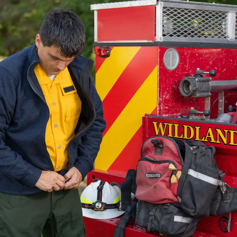 Red True North Gear Fireball™ Pack resting on the back of a fire truck as a firefighter prepares equipment, showcasing the pack’s rugged design and ready accessibility during emergency response.