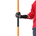 Close-up of a gloved hand gripping the black foam middle section of the Northern Diver Telescopic Wading Pole, with a rescue technician in a red drysuit standing beside it.