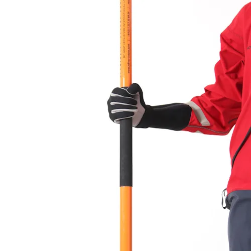 Close-up of a gloved hand gripping the black foam middle section of the Northern Diver Telescopic Wading Pole, with a rescue technician in a red drysuit standing beside it.