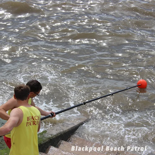 Blackpool Beach Patrol lifeguards extending the Northern Diver Shepherd's Crook Reach Pole Attachment with orange buoy attachment over rough water toward the shoreline.