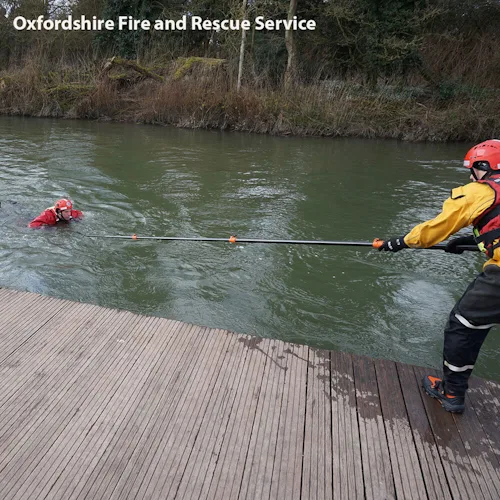 Oxford Fire rescuer on a wooden jetty extending a Northern Diver reach pole to a swimmer in the water.