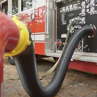 Black Kochek PVC suction hose with Storz swivel coupling connected to a fire truck pump panel at a hydrant.